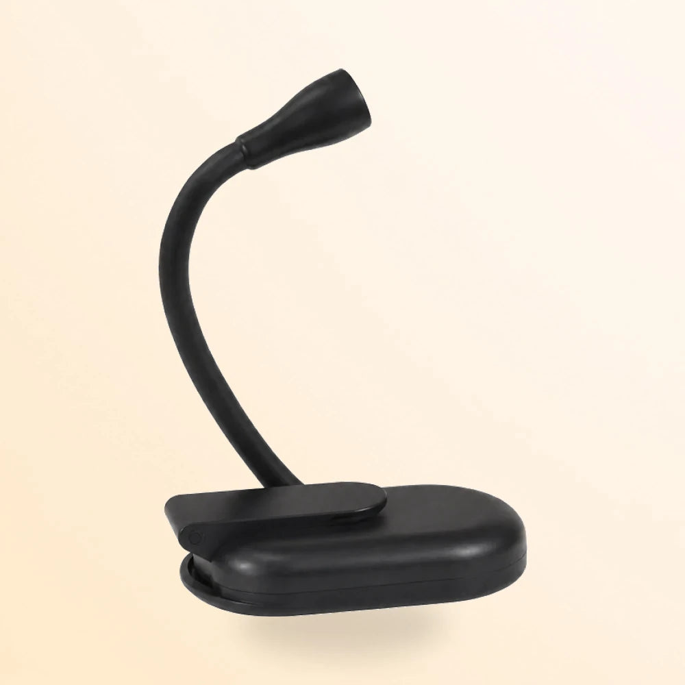 Petite lampe noire à pince posée sur un bureau à côté d'un livre ouvert éclairé
