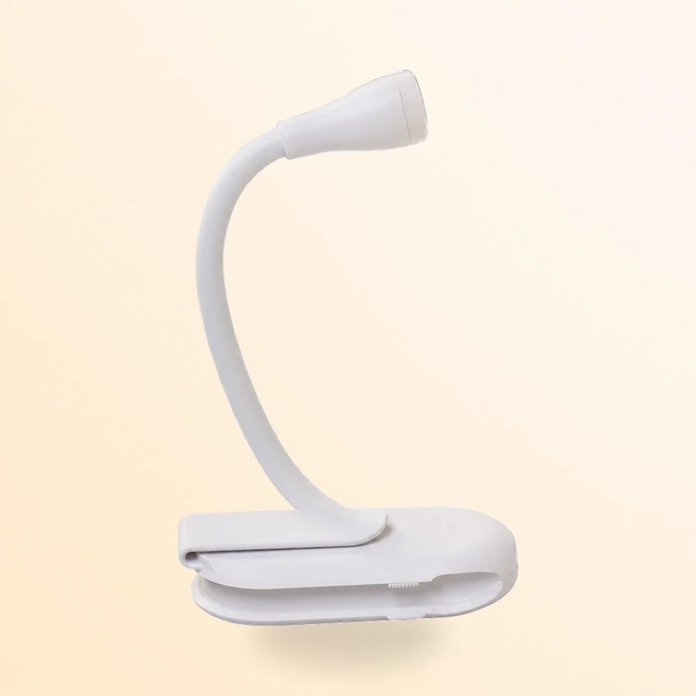 Petite lampe blanche à pince posée sur un bureau à côté d'un livre ouvert éclairé