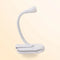Petite lampe blanche à pince posée sur un bureau à côté d'un livre ouvert éclairé