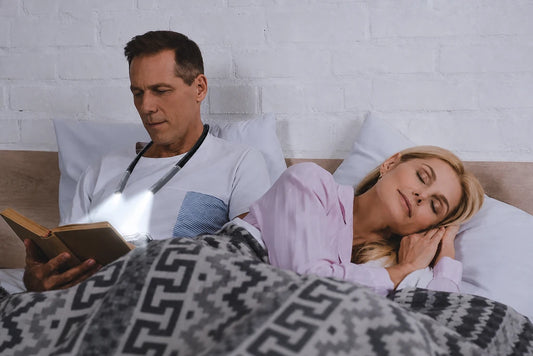 Homme lisant la nuit avec une lampe de cou sans déranger son partenaire endormi