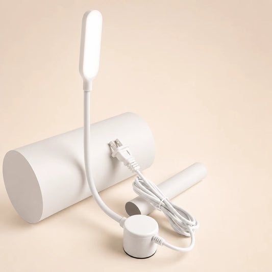 Lampe flexible blanche posée sur un cylindre blanc, doigt appuyant sur le bouton variateur trois vitesses