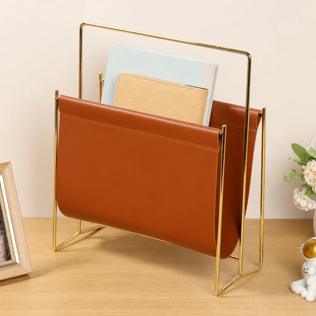 Porte-revues en simili cuir caramel sur cadre doré, posé sur un bureau en bois avec magazines et livres