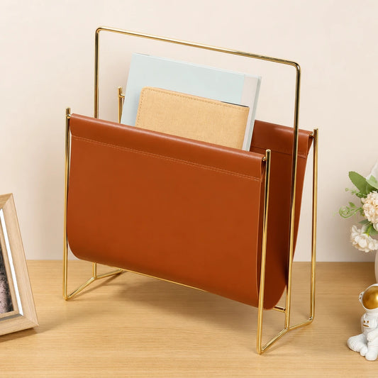 Porte-revues en simili cuir caramel sur cadre doré, posé sur un bureau en bois avec magazines et livres