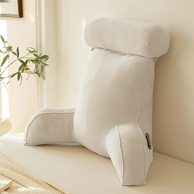 coussin de lecture blanc posé contre un mur, près d’une plante verte