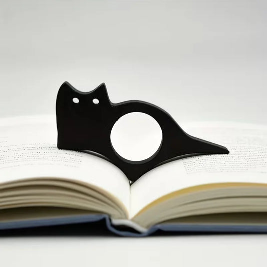 Accessoire noir en silhouette de chat maintenant les pages d’un livre ouvert