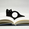 Accessoire noir en silhouette de chat maintenant les pages d’un livre ouvert