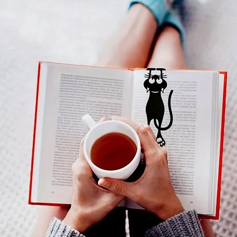 Chat noir dans un livre ouvert devant une tasse tenue à deux mains