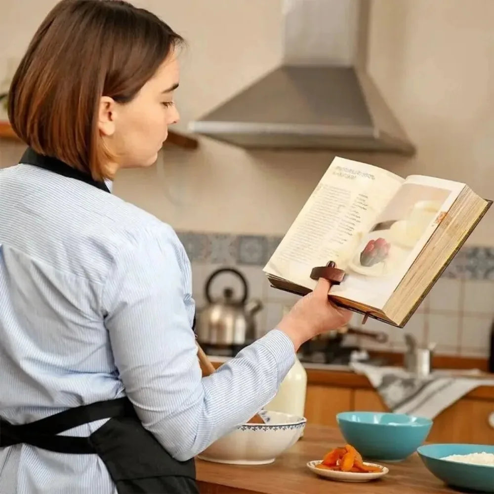 Femme tenant un livre de cuisine ouvert à l'aide d'un support passé au pouce